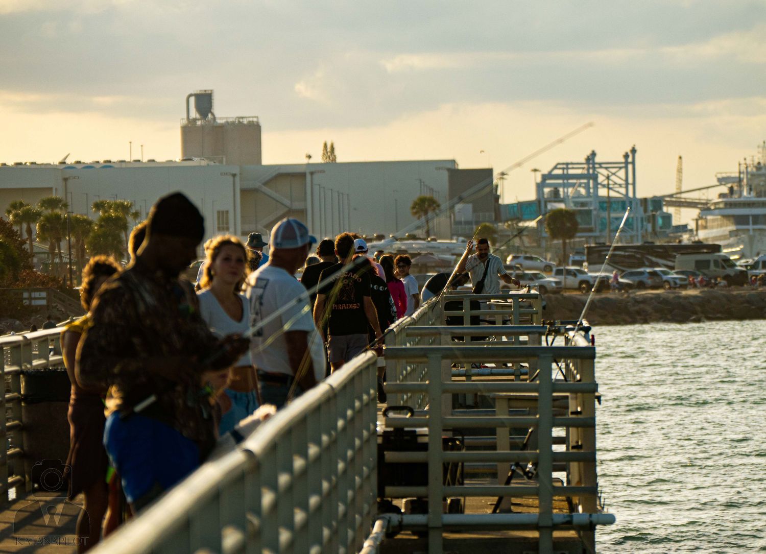 People gather on a wooden pier overlooking boats and water during sunset at a marina.