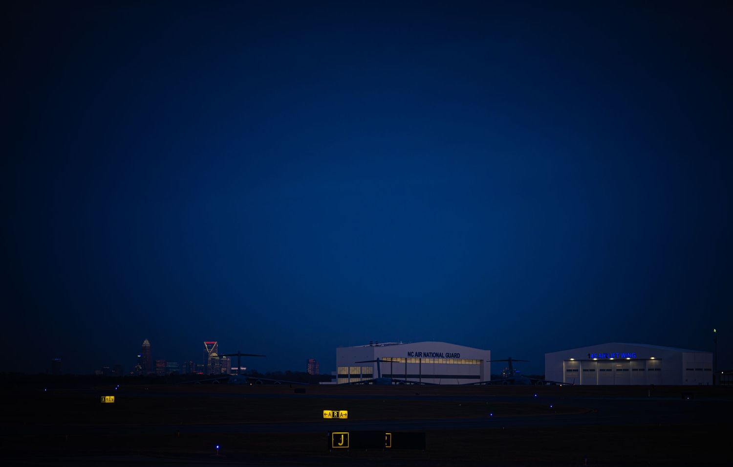 Dark night sky with distant city lights and buildings silhouetted against a deep blue horizon.