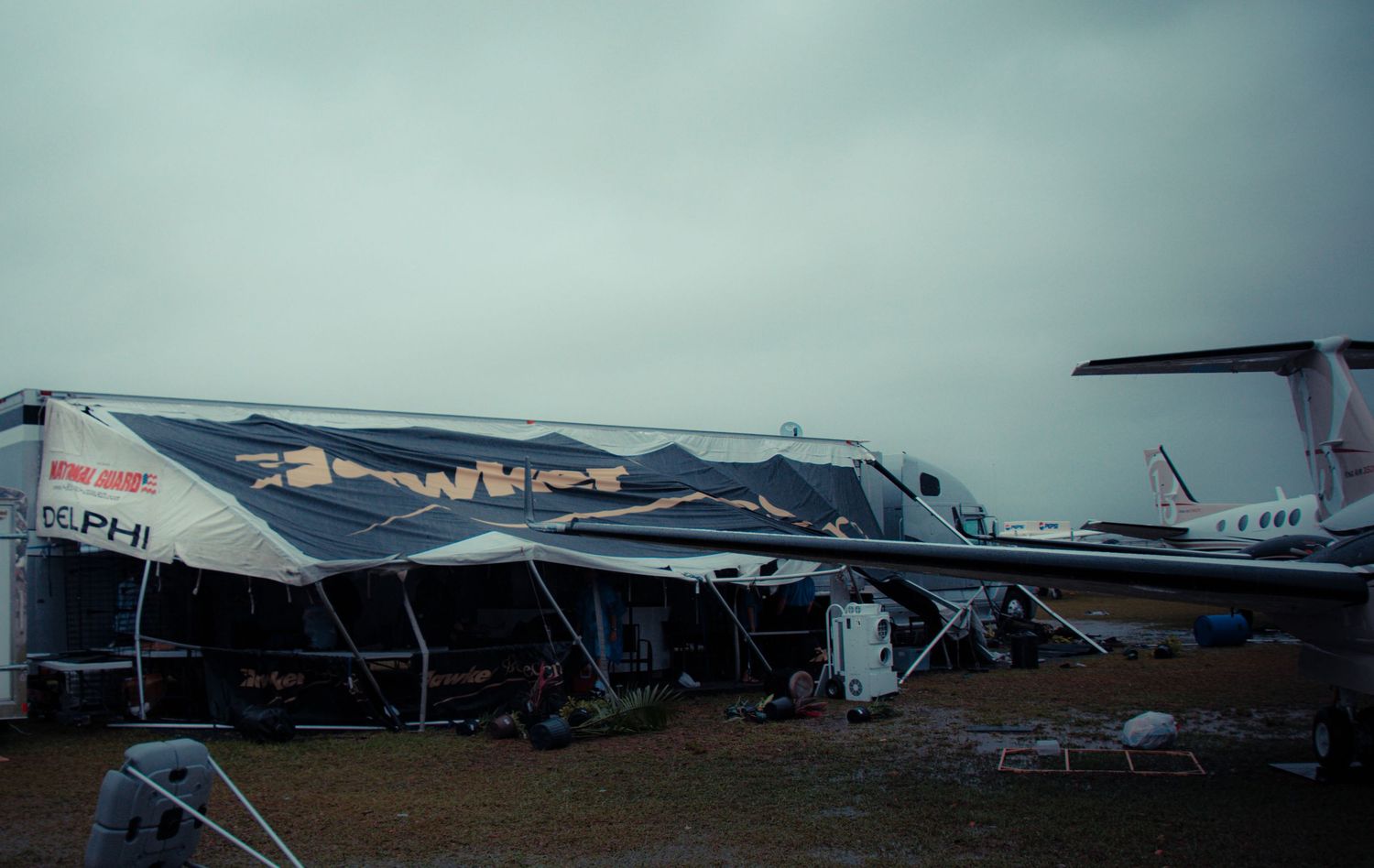 Multiple damaged aircraft and debris scattered across an airfield after what appears to be storm damage.
