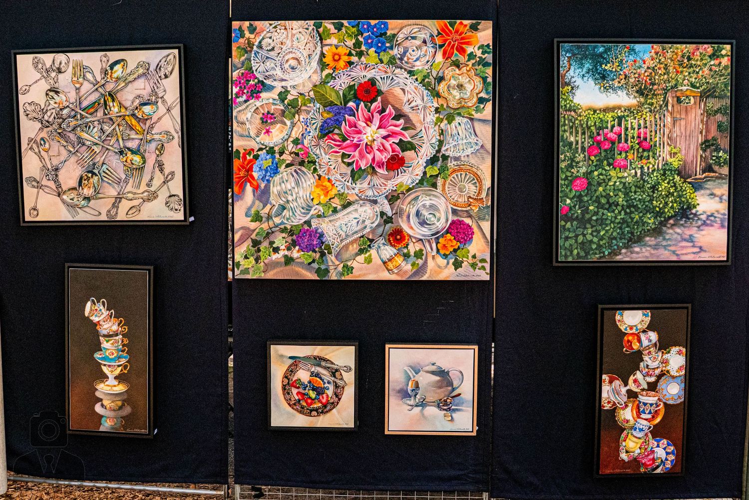 Colorful artwork and paintings displayed in a gallery setting with black walls and lighting.