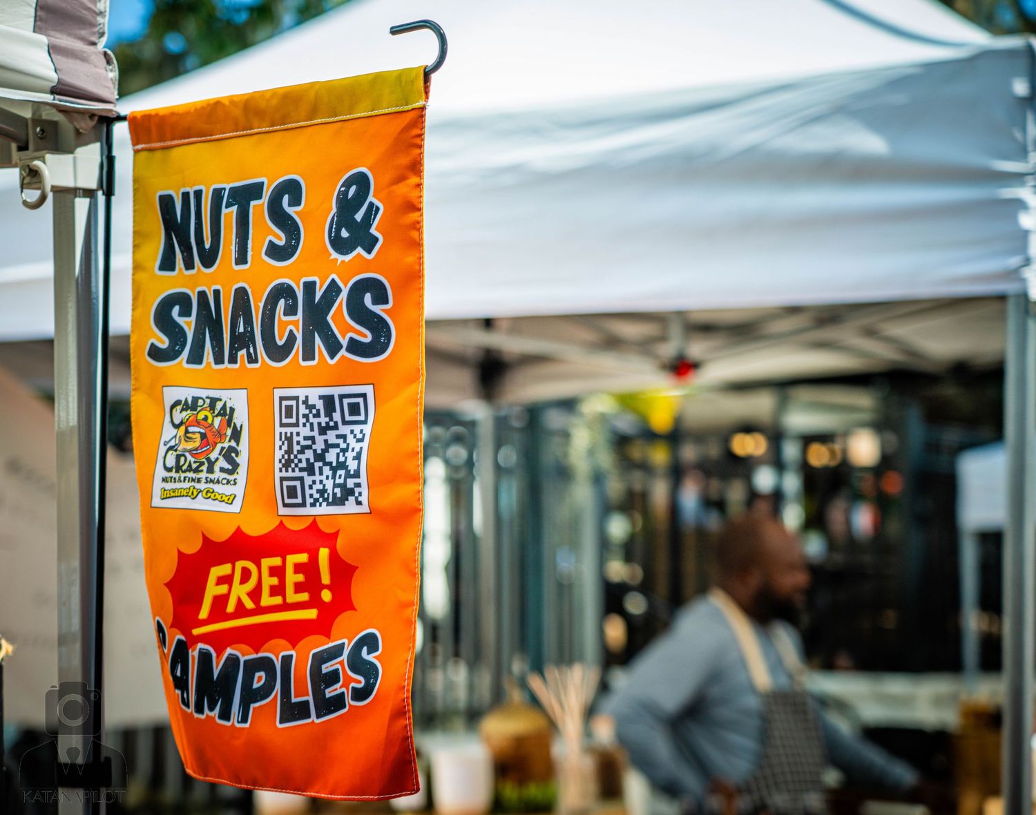 Orange banner advertising nuts and snacks with free samples and QR codes at an outdoor market stall.