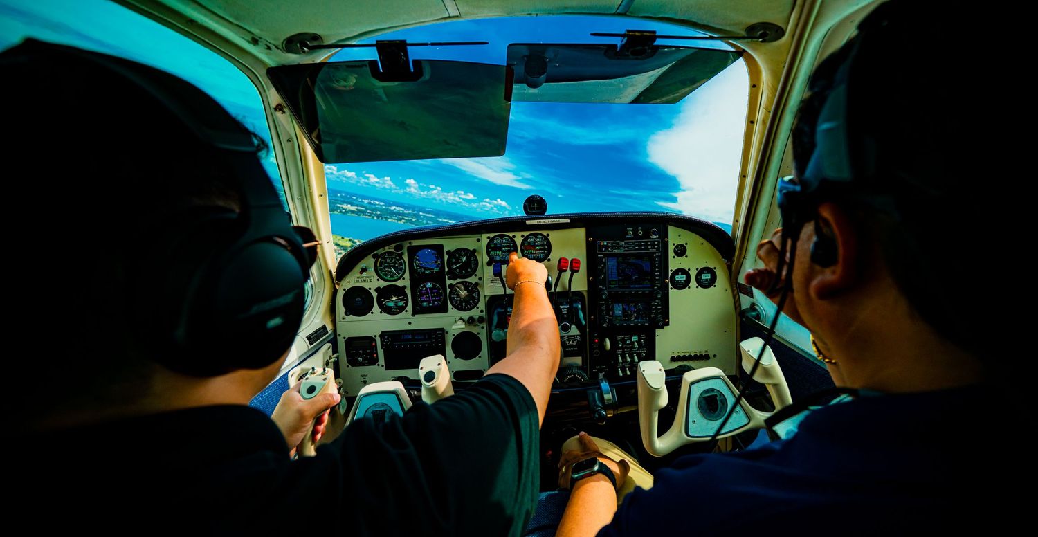 Cockpit view of small aircraft showing flight instruments and blue sky through windscreen.