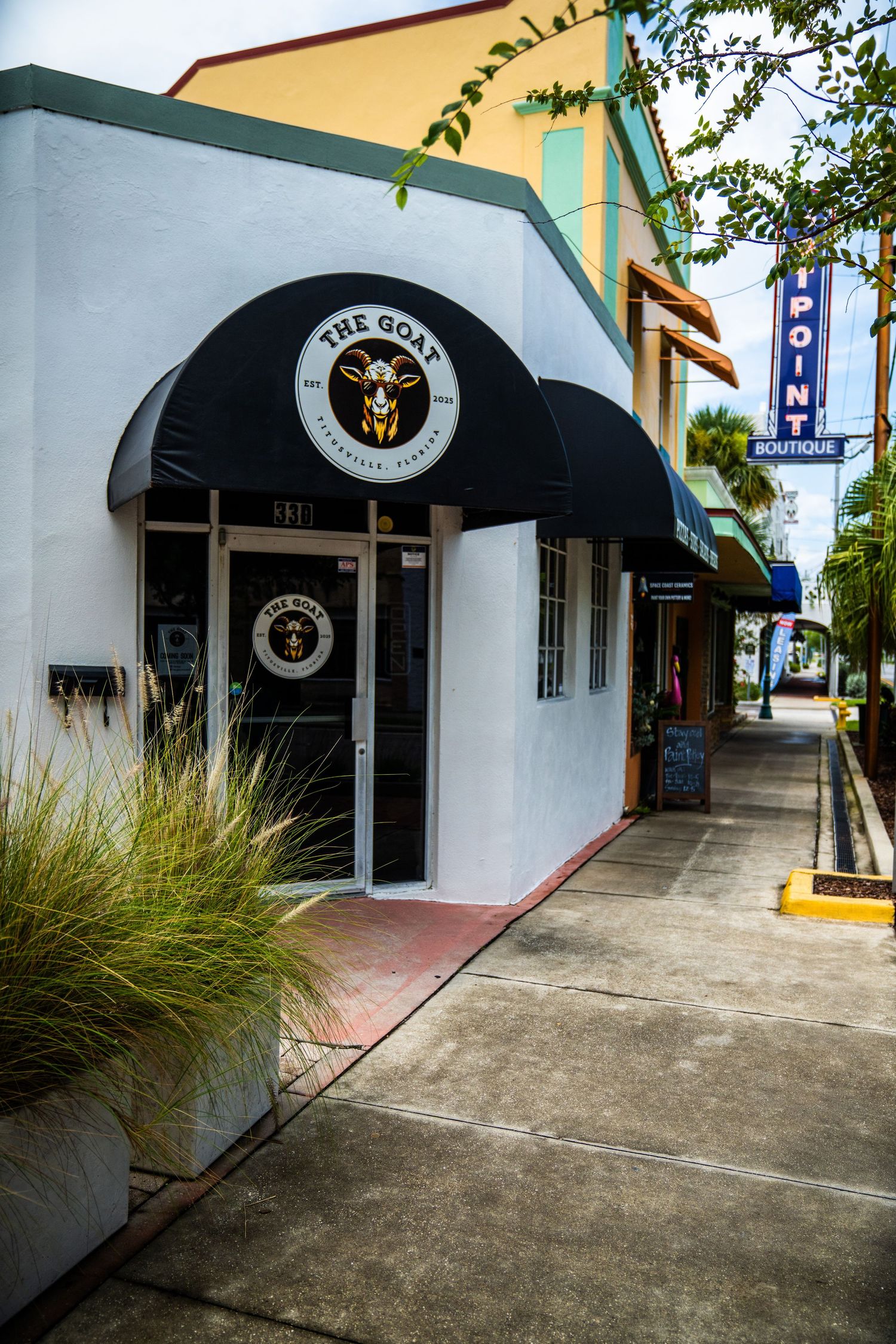 Series of storefronts with black awnings and concrete walkway in a shopping center.