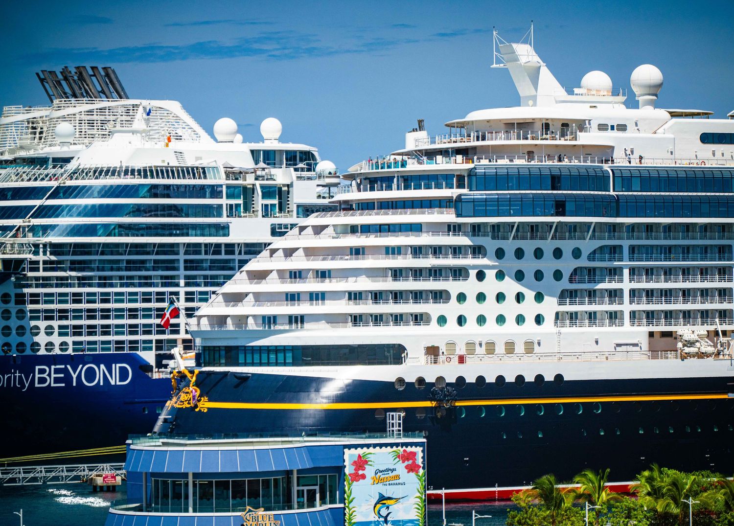 Two large cruise ships docked at a colorful Caribbean port on a sunny day.