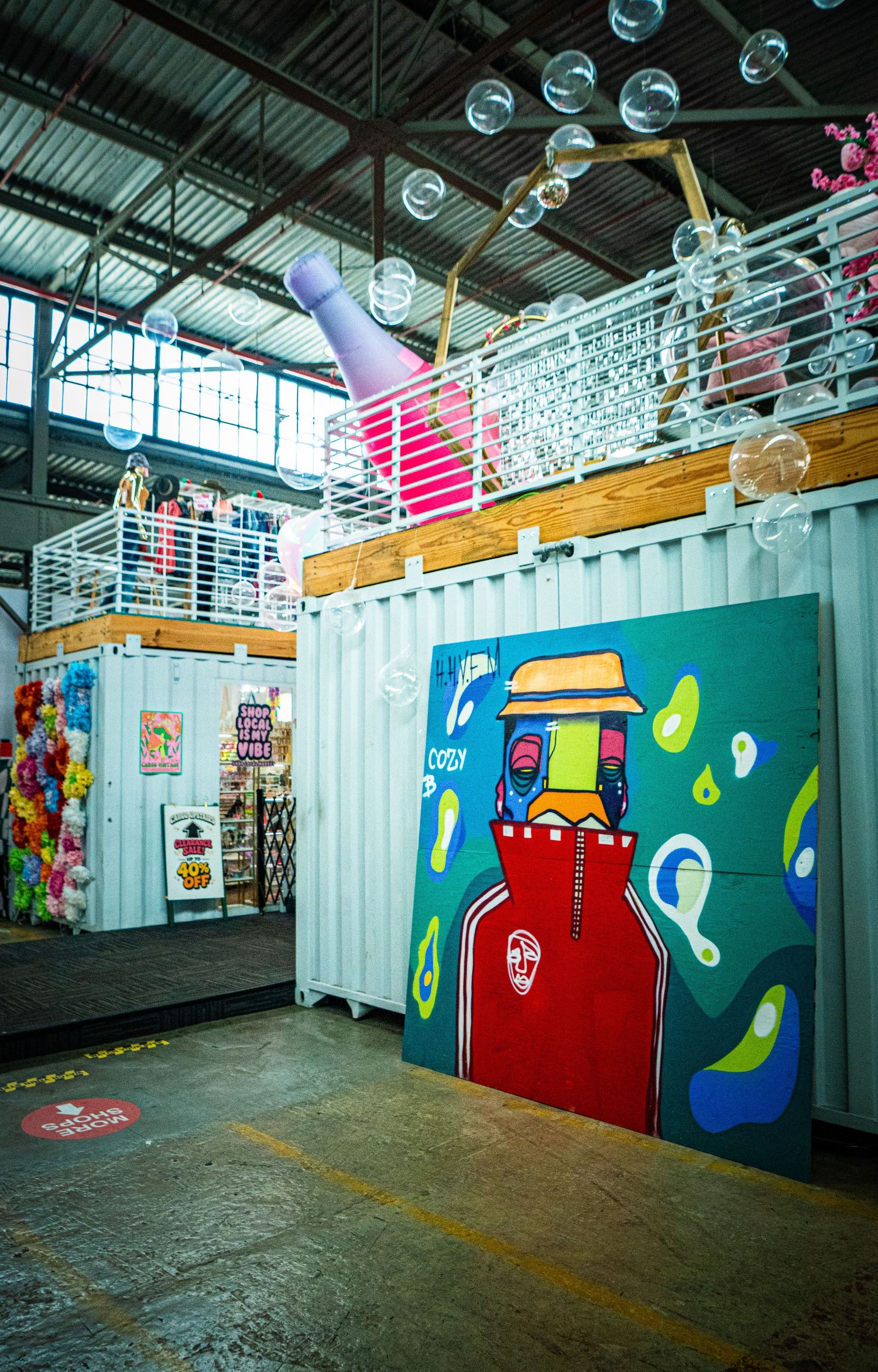 Colorful shipping container art installation with bubble decorations and vibrant street art mural inside an industrial warehouse space.