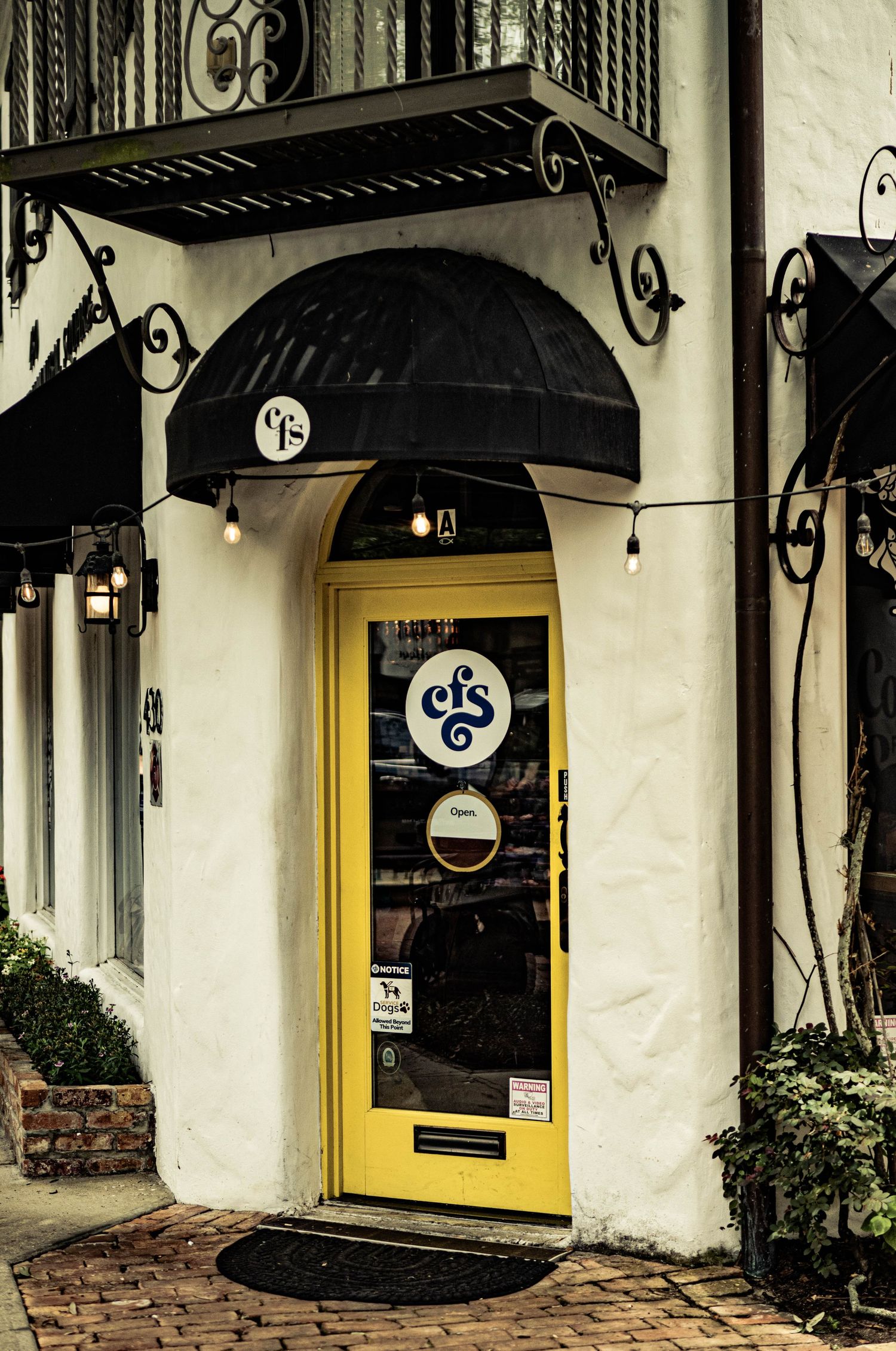 Charming storefront with a bright yellow door, black awning, and decorative ironwork on a white brick building.
