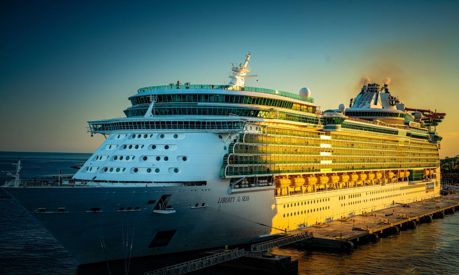 Large cruise ship docked at port during golden sunset with dramatic sky in the background.
