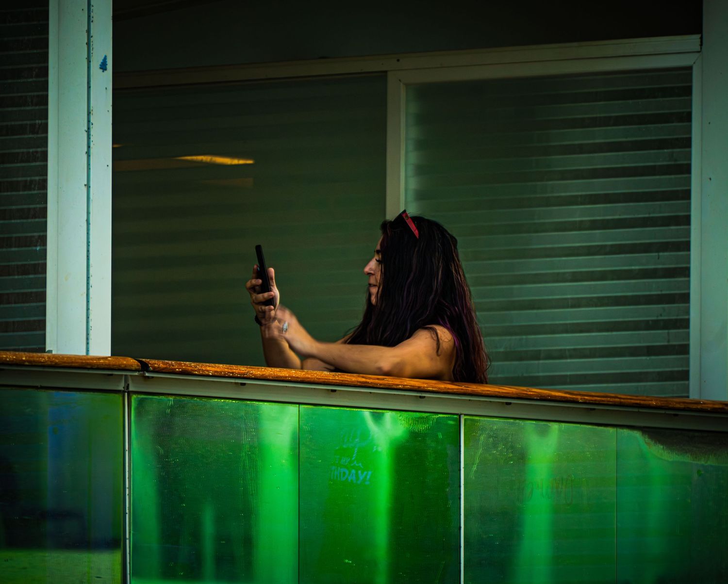 Person using phone on balcony at night with green ambient lighting illuminating the scene.