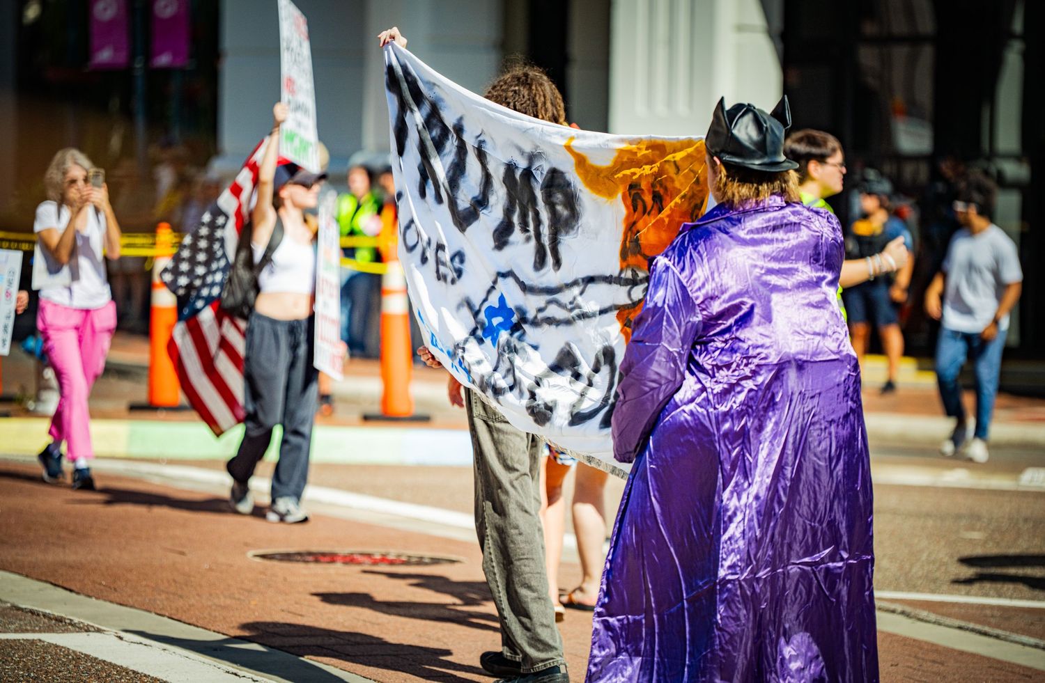 Purple banners and protest signs line an urban sidewalk during a demonstration.