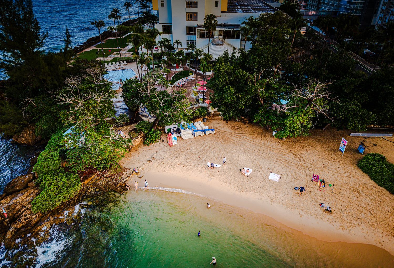 Aerial view of a secluded beach cove surrounded by lush tropical vegetation and resort buildings in Hawaii.