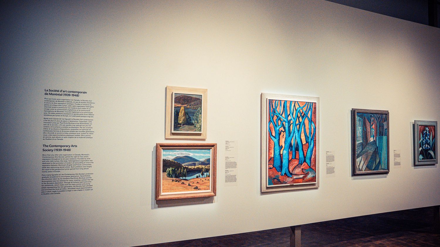 Art gallery wall displaying colorful modern paintings in a clean white exhibition space.