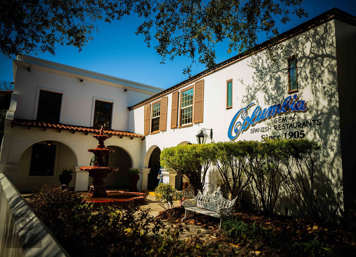 Panoramic view of Spanish colonial architecture with white stucco walls and red tile roofs under blue sky.