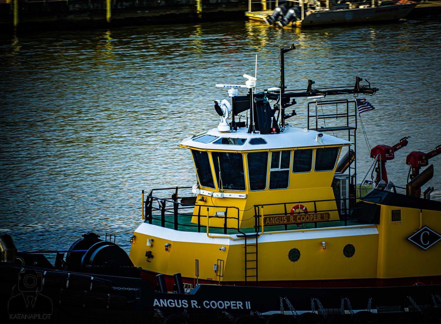 A sequence of yellow tugboats lined up along a waterfront dock with calm blue water in the background.