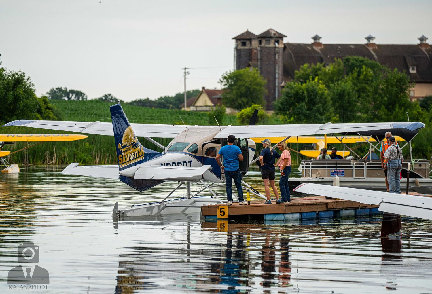 Seaplane passengers board from a wooden dock while parked at a waterfront facility.