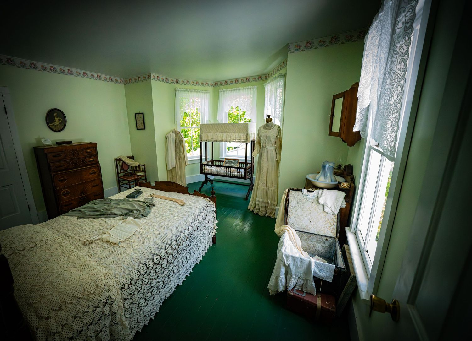 Victorian bedroom with green painted floors, white lace curtains, and antique furnishings.