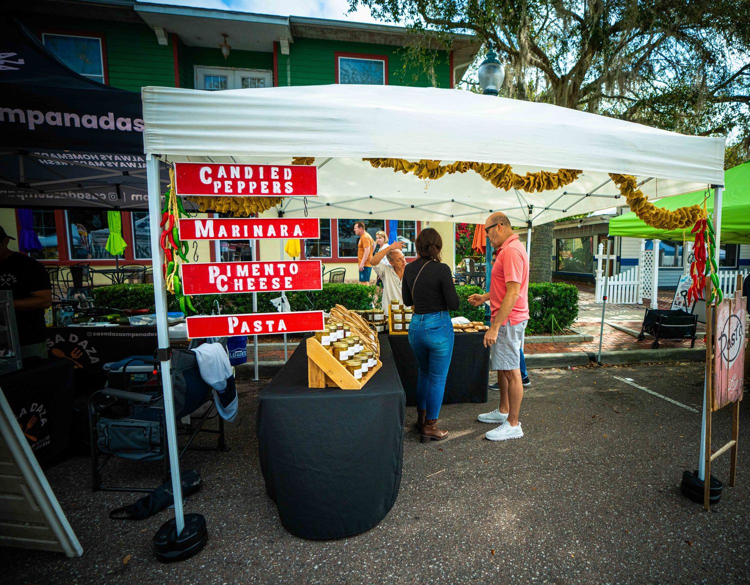 Outdoor market vendors set up white tents and food stalls at a local farmers market or street fair.