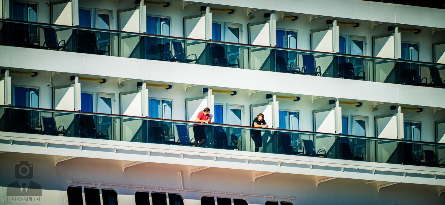 Modern cruise ship balconies and windows line the side of a massive vessel in daylight.