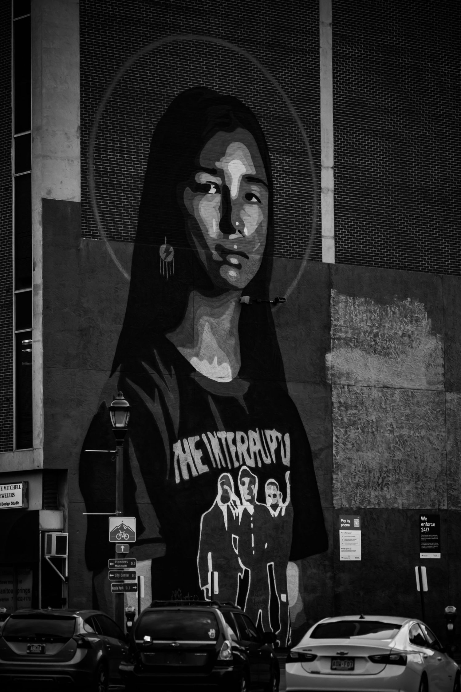 Black and white photo of a large street mural depicting a woman wearing a The Interrupters band t-shirt on a city building.