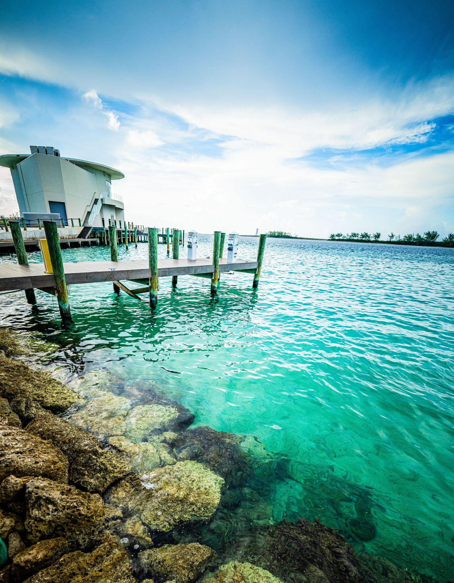 Turquoise waters surround a wooden dock near a modern building under a bright blue sky in the Florida Keys.