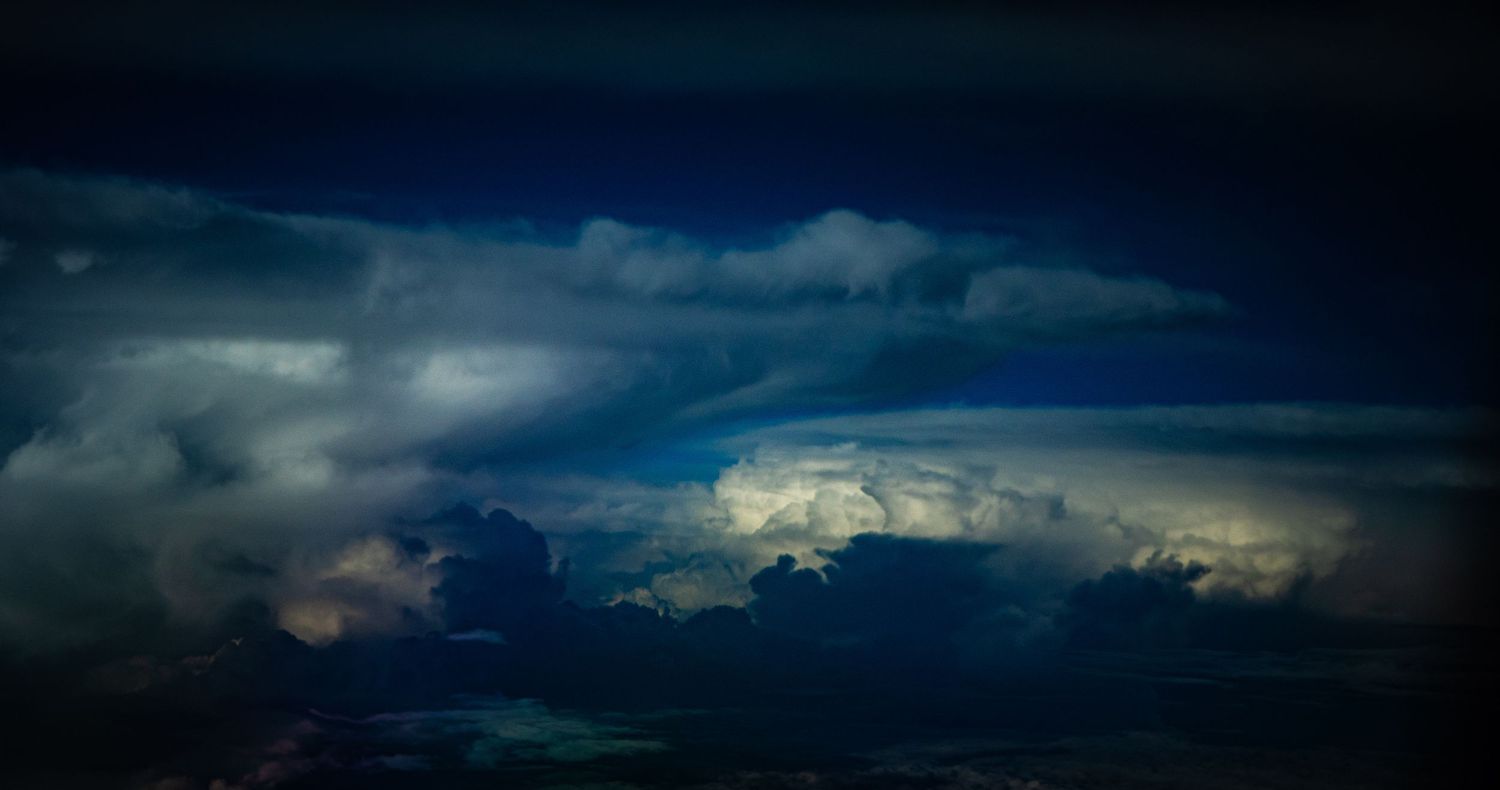 Dramatic stormy sky with towering cumulonimbus clouds illuminated from within against a dark blue twilight atmosphere.