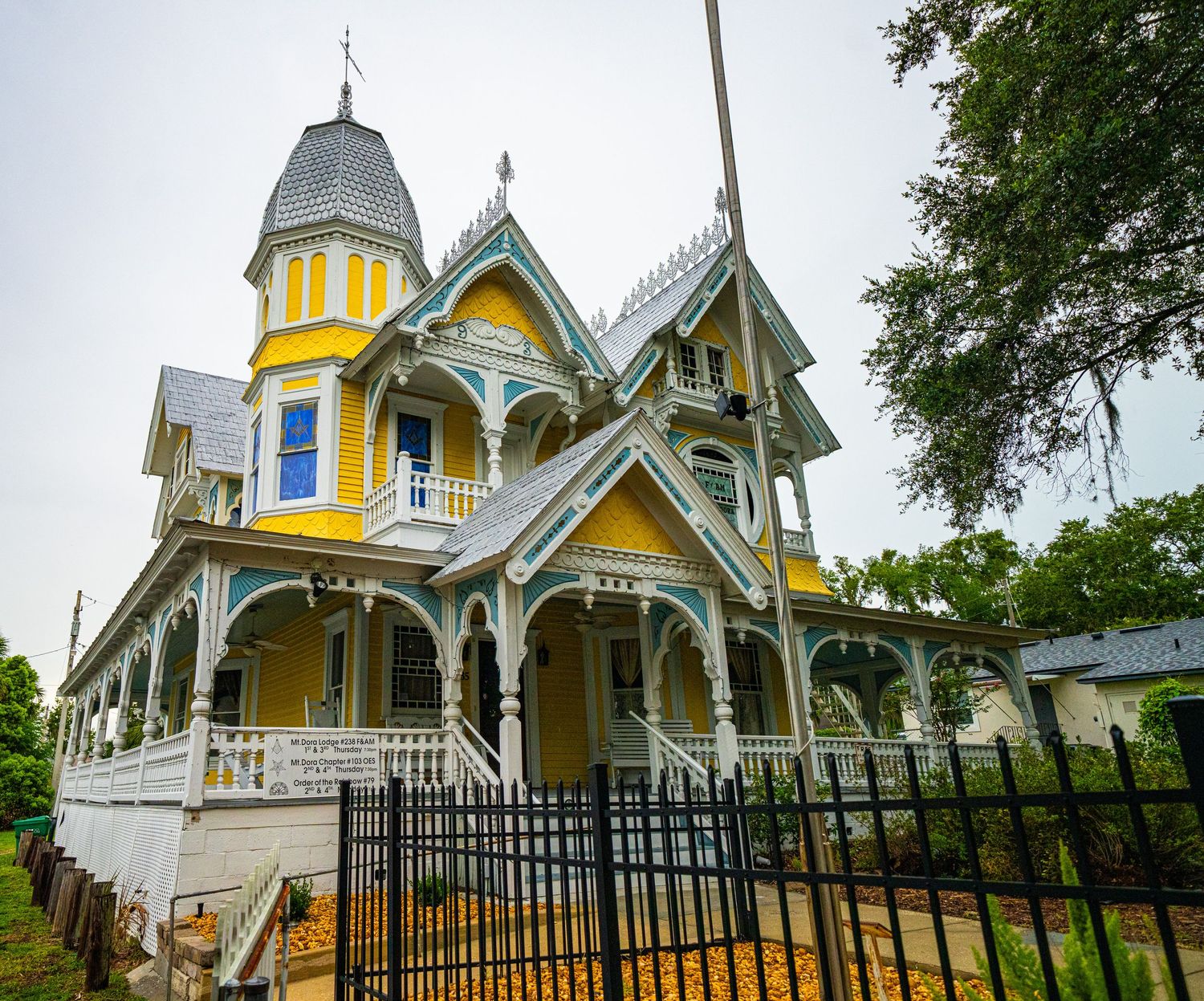 Victorian-style yellow house with ornate architectural details and black iron fence.