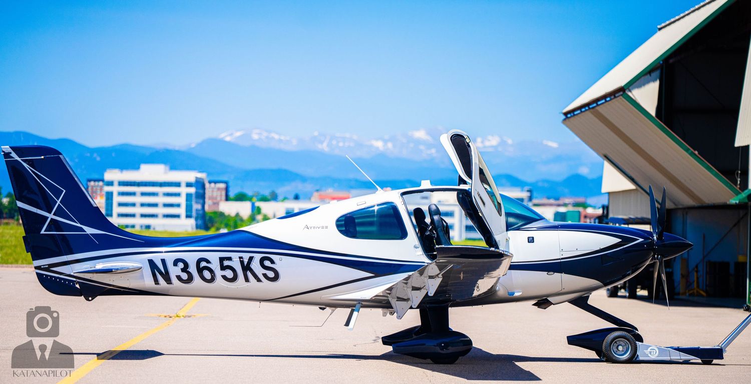 Row of small private aircraft parked on sunny tarmac with blue sky.
