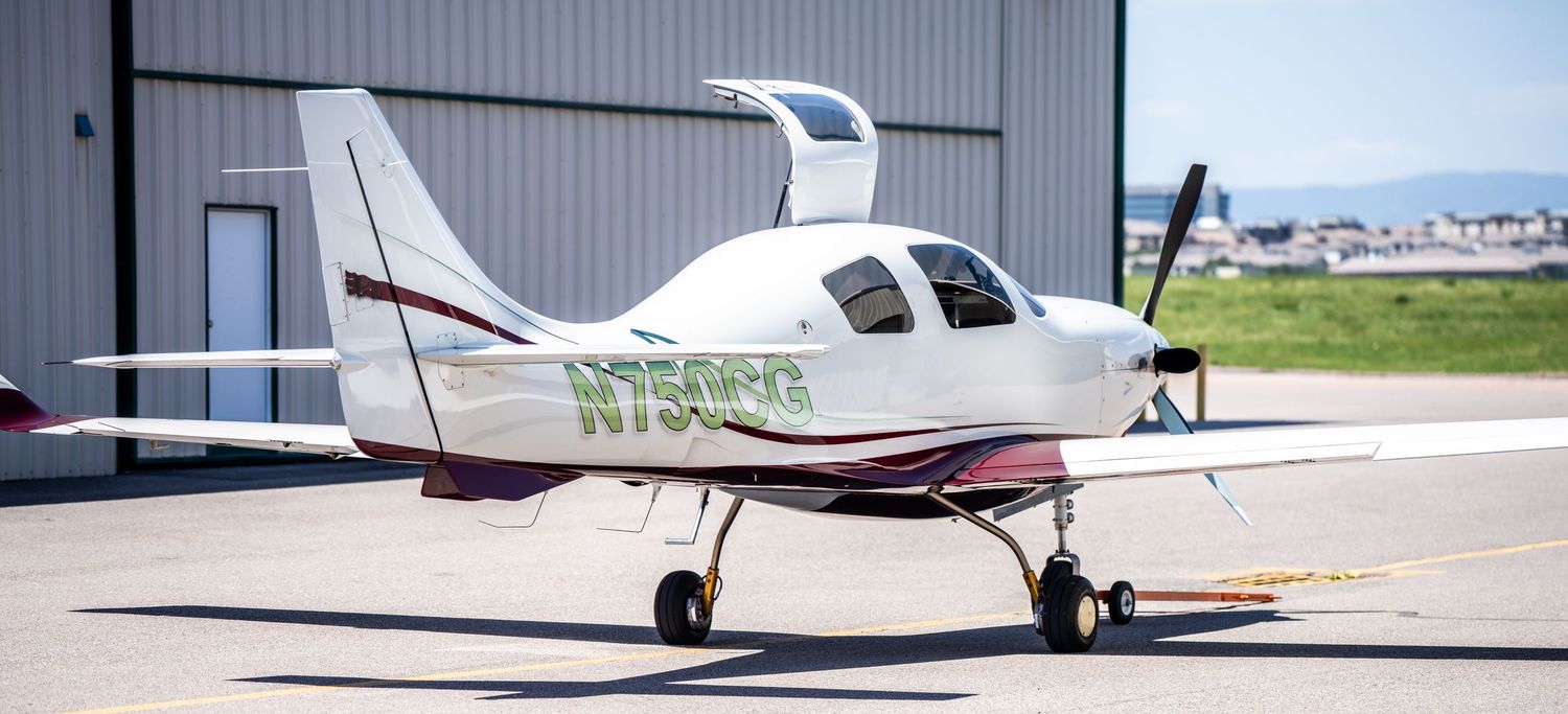 Row of small private aircraft parked outside hangar on sunny day.