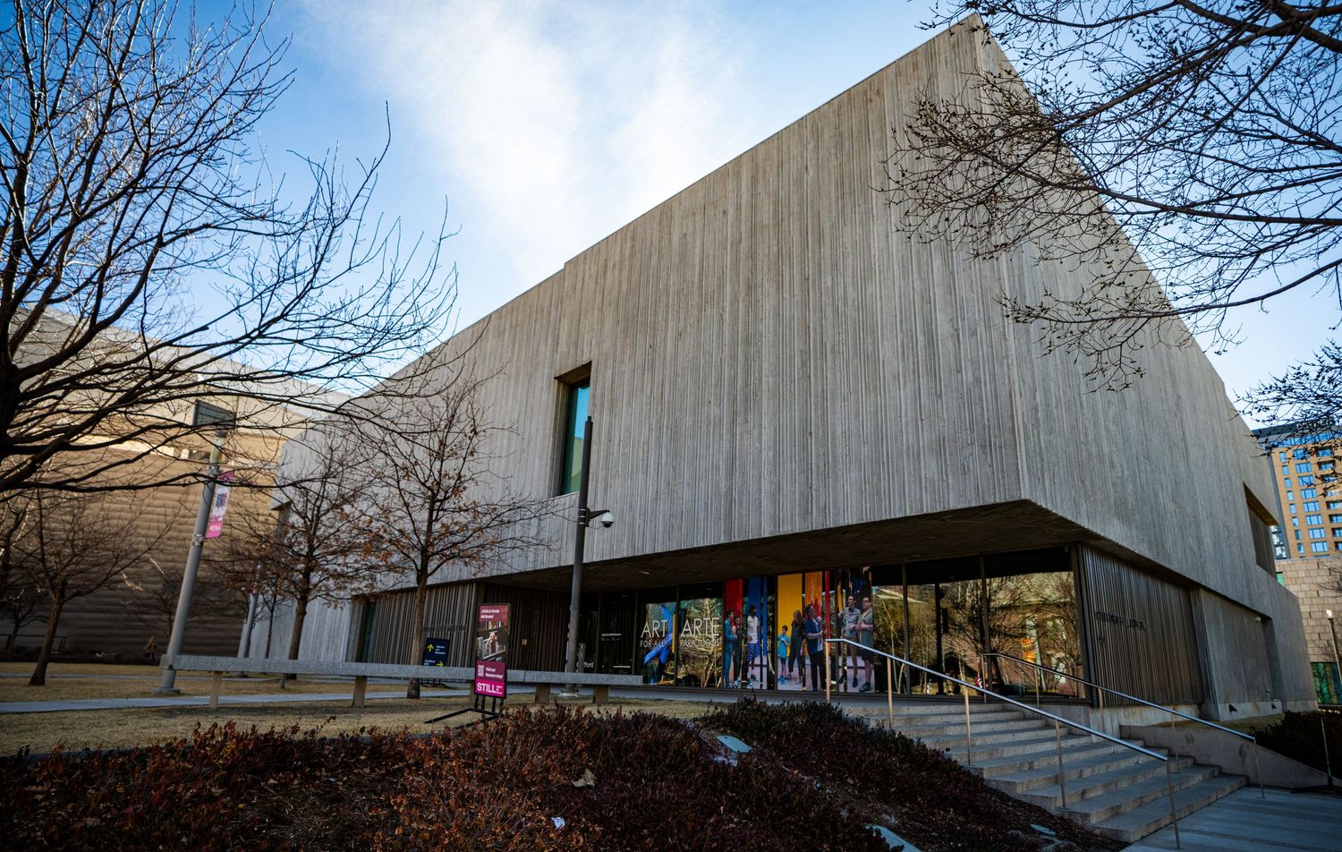 Modern concrete building with angular architecture and glass windows set against bare winter trees on a hillside.