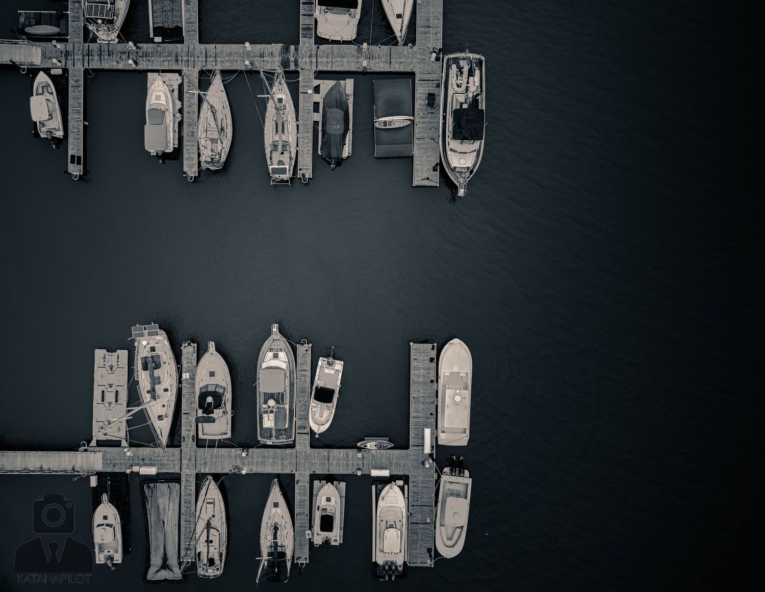 Aerial view of boats and yachts docked in a marina at night creating geometric patterns against dark water.