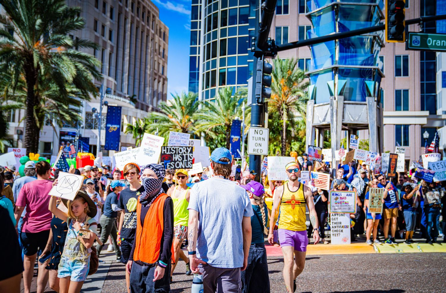 Large crowd gathering in urban area with palm trees and office buildings in background.