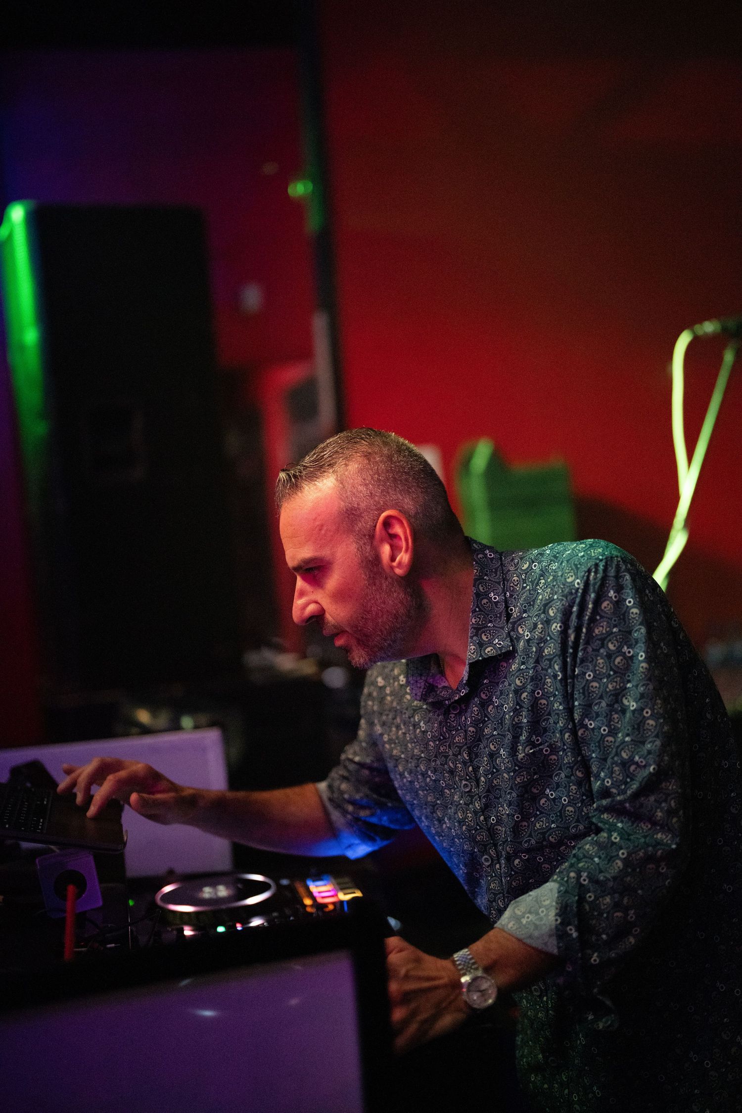 DJ works the turntables under moody red and green lighting at a nightclub.