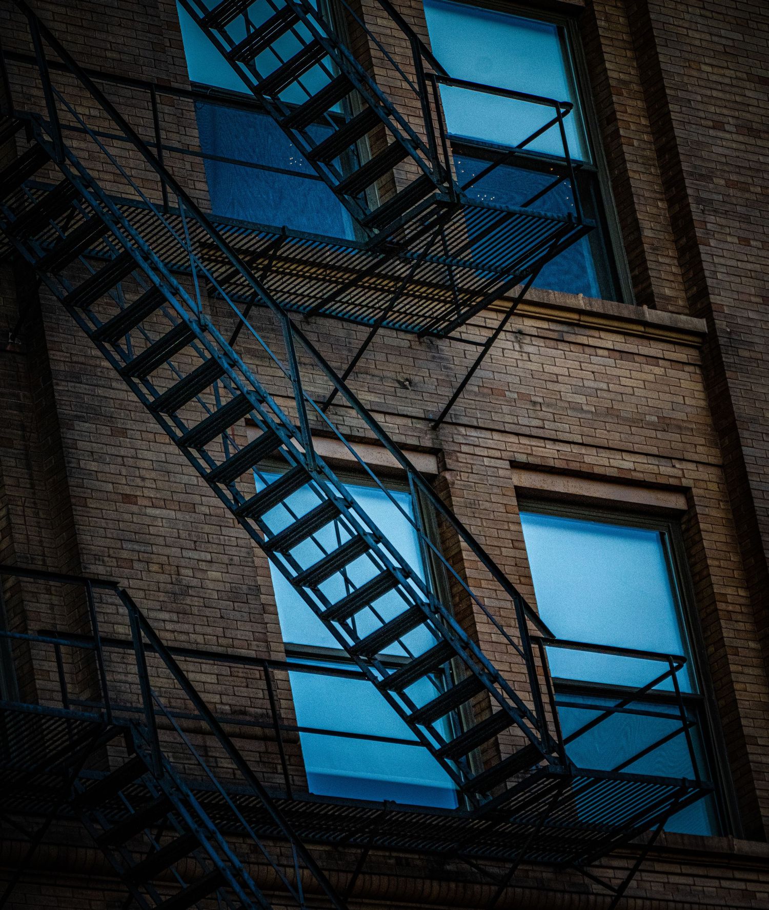 Fire escape stairs and windows on brick building with dramatic shadows.