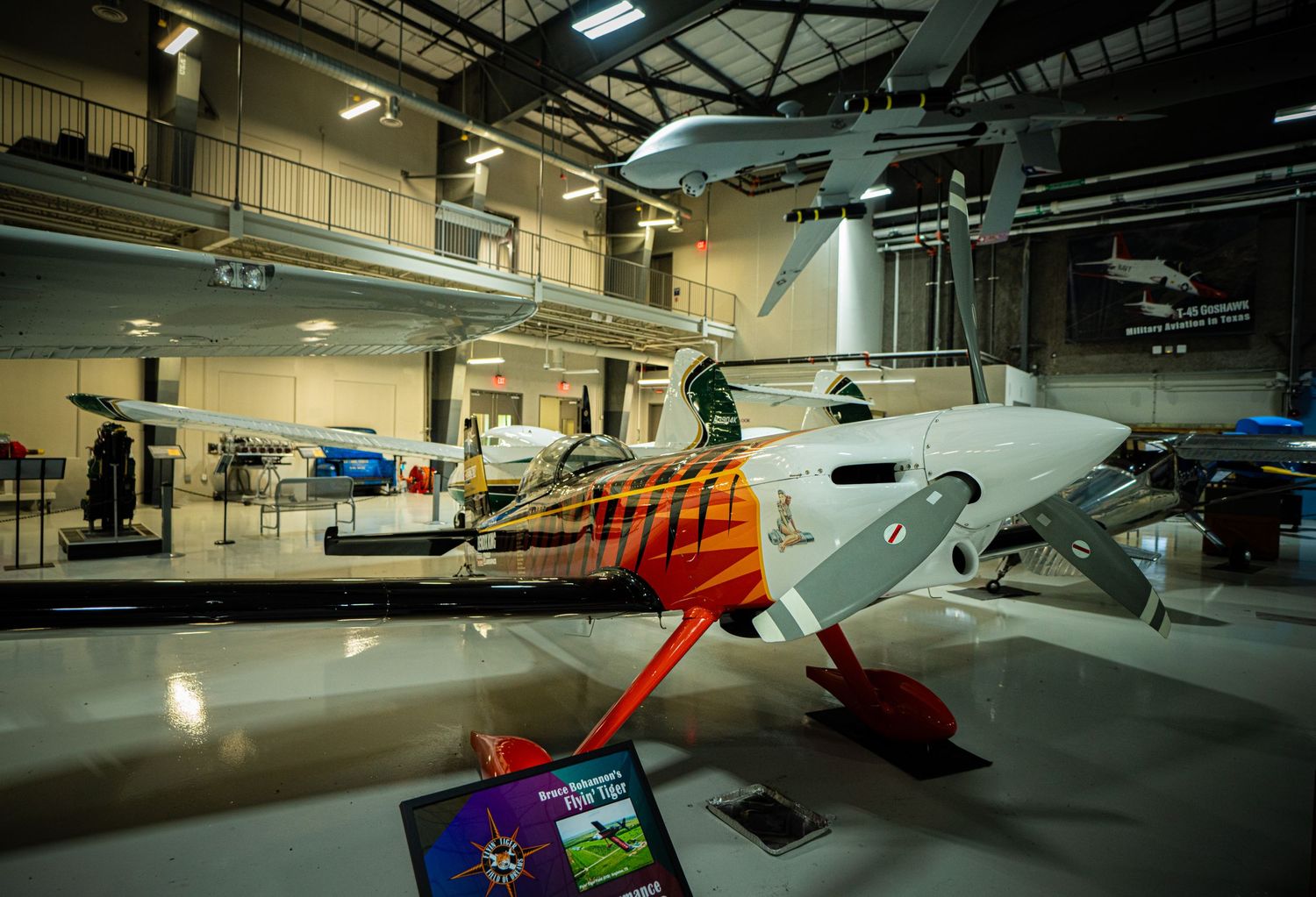 Colorful aerobatic stunt plane with orange markings on display inside a modern aviation museum.