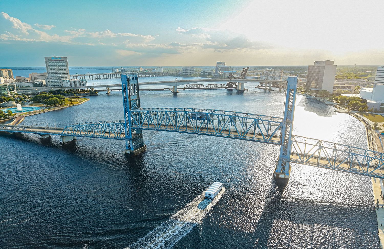 Aerial view of a blue drawbridge over a wide river in Jacksonville, Florida, with a boat passing beneath at sunset.