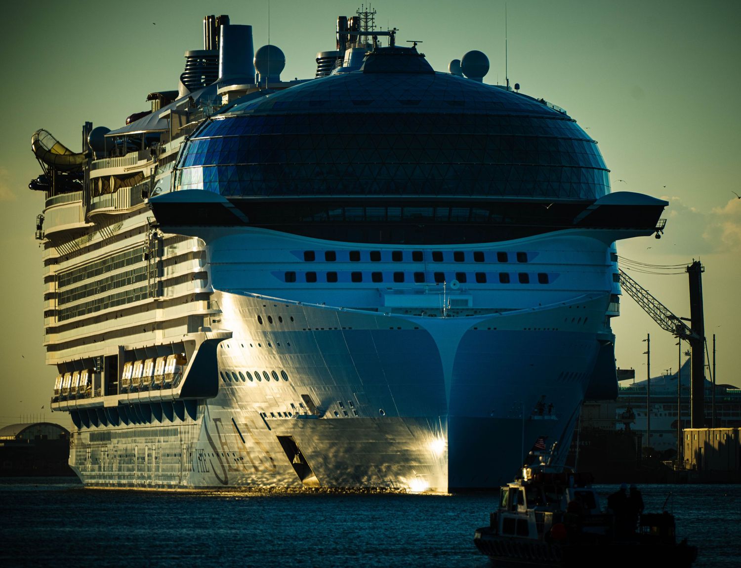Luxury cruise ship silhouetted against sunset with dramatic lighting and reflective hull details.