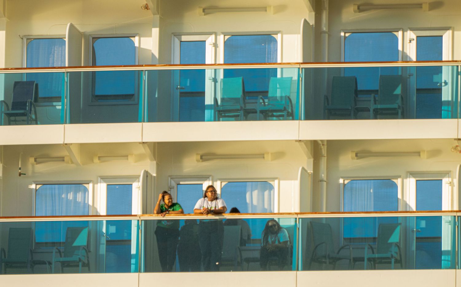 Modern apartment building exterior with glass balconies and blue-tinted windows reflecting sunlight.
