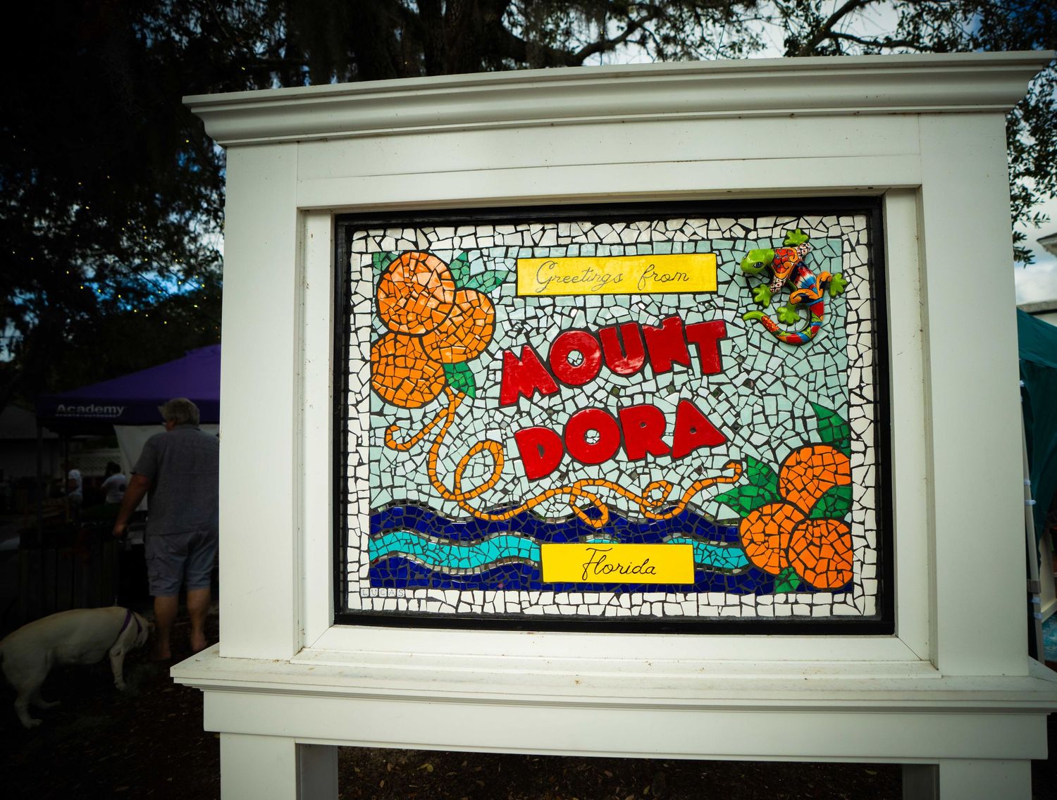 A series of colorful mosaic art panels with text displayed on white frames mounted on an outdoor wall.