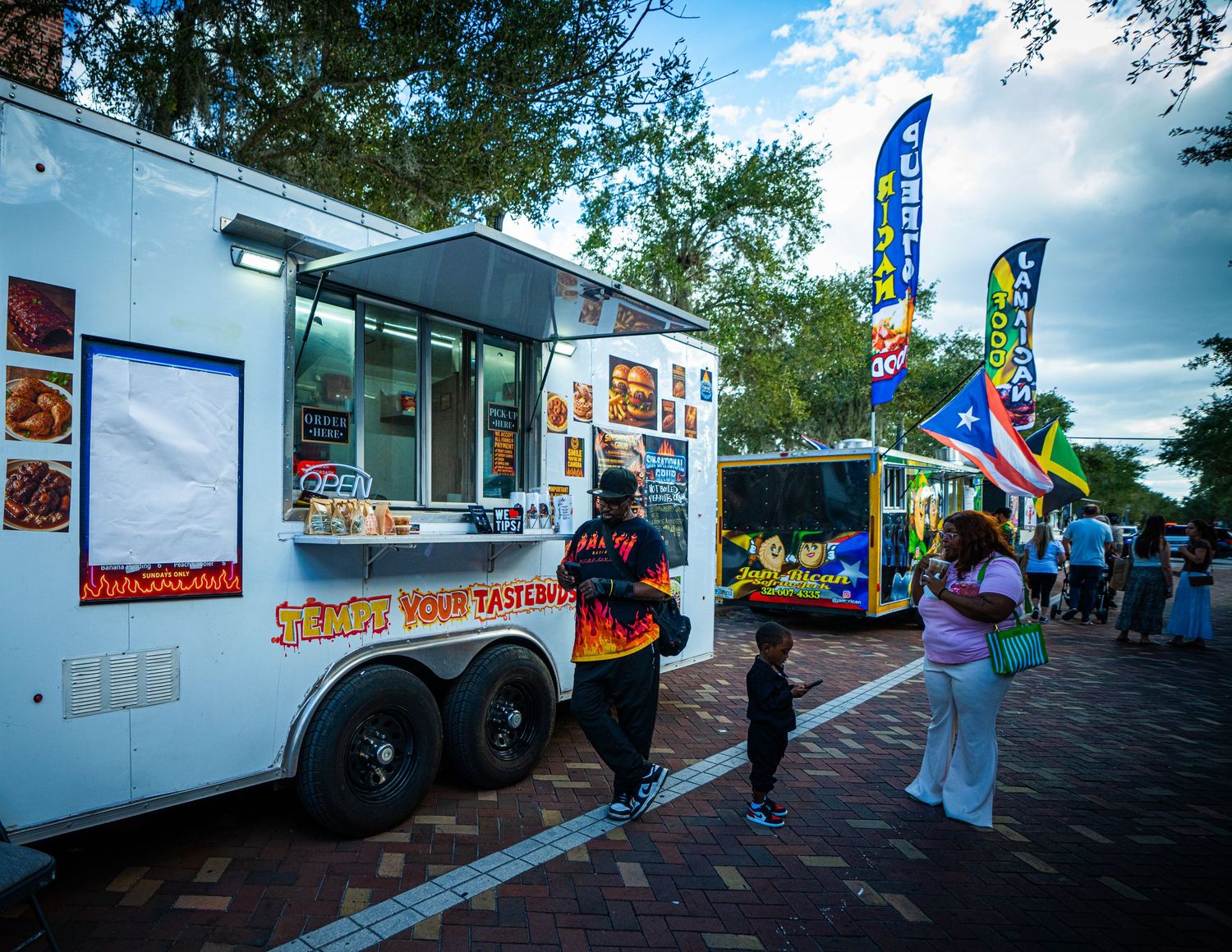 Food truck serving customers on a brick paved street with colorful feather flags waving in the breeze.
