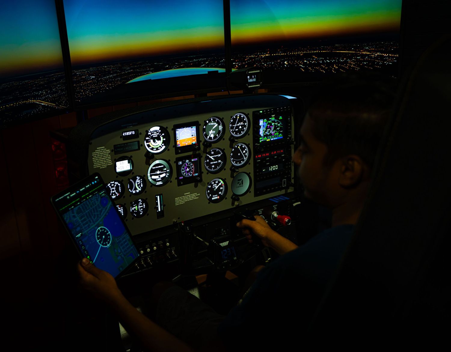Two pilots training in a flight simulator cockpit at night with illuminated instrument panels.
