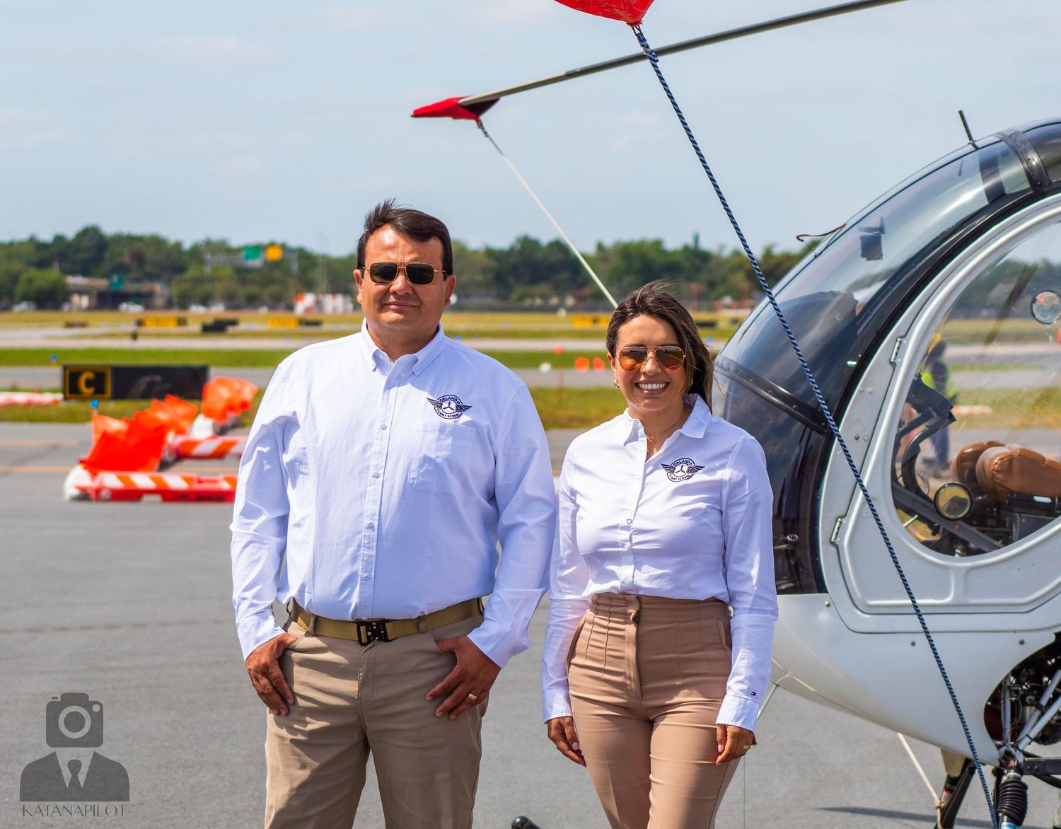 Professional aviation crew standing beside white helicopter on airfield.