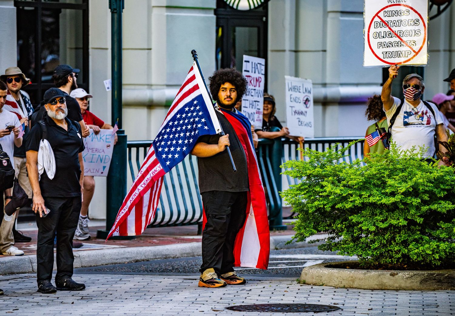 Demonstrator holding American flag during protest gathering outside urban building.
