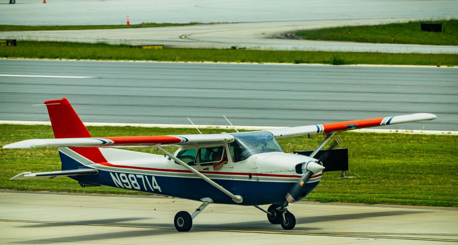 Small red and white Cessna aircraft N98714 taxiing on airport runway, single-engine propeller plane on tarmac.