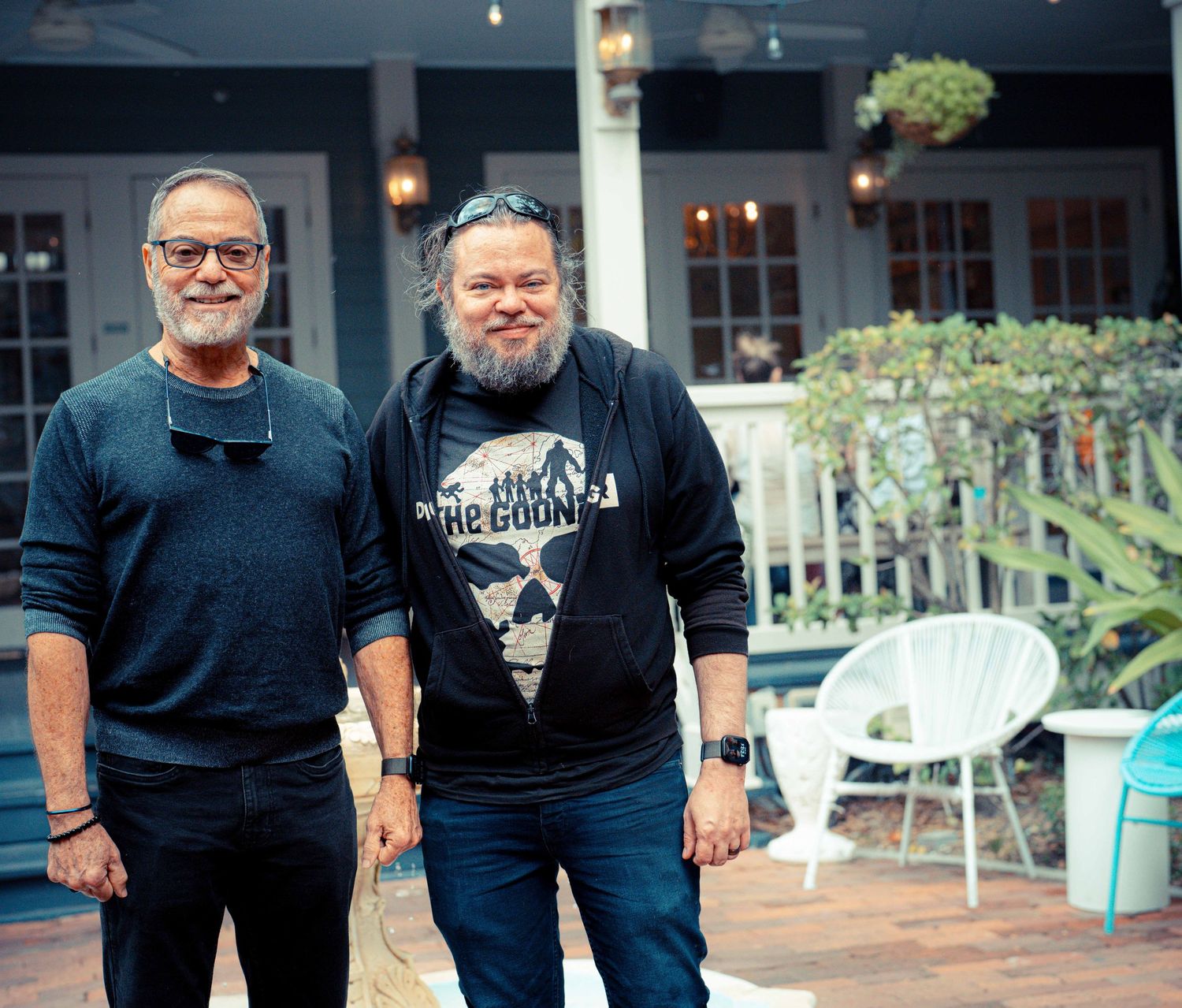 A group of people wearing dark clothing stand together on a patio with hanging lights and outdoor furniture.