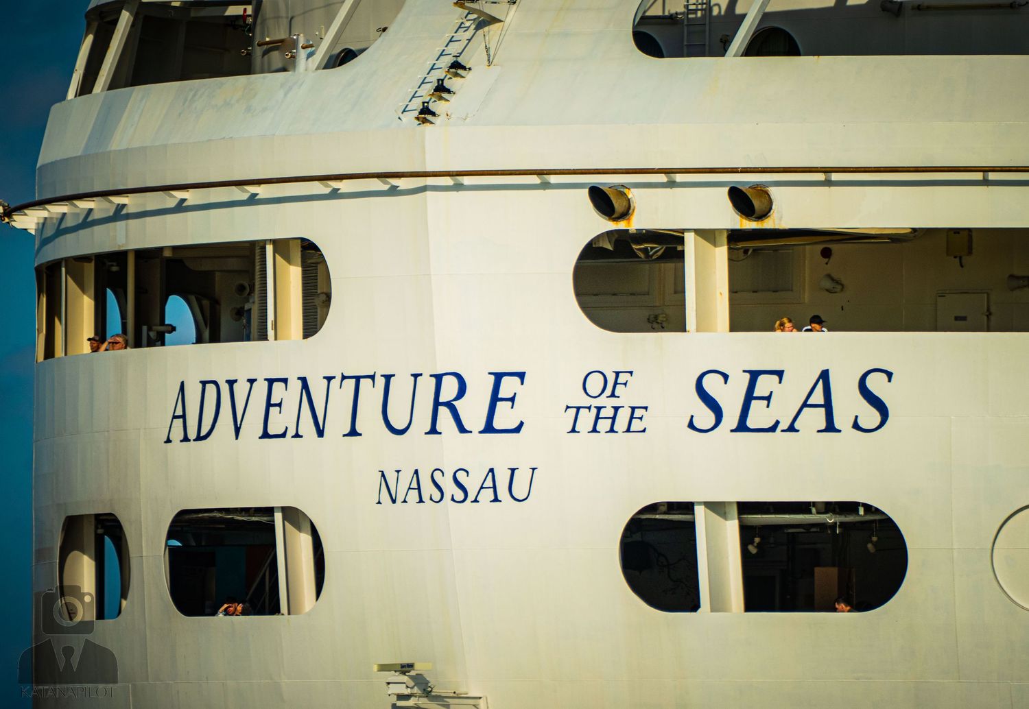 Side view of a white cruise ship hull with text 'Adventure of the Seas' and 'Nassau' painted on its side.
