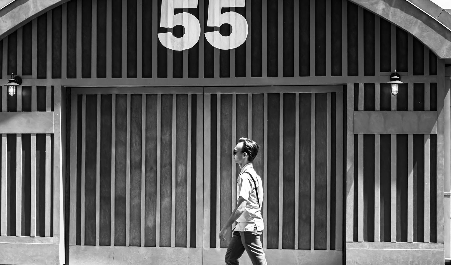 Black and white photograph of vintage horse stalls with numbers and vertical bars in a rustic barn setting.
