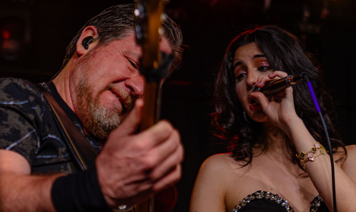 Male guitarist and female vocalist performing live on stage under warm lighting at a concert.