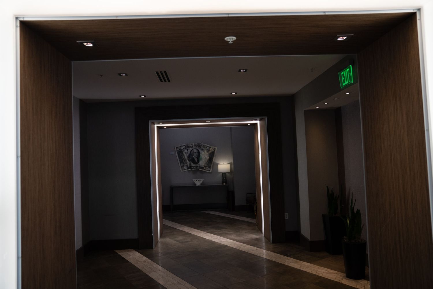 Long dark corridor with wooden panels and minimal lighting in commercial building.