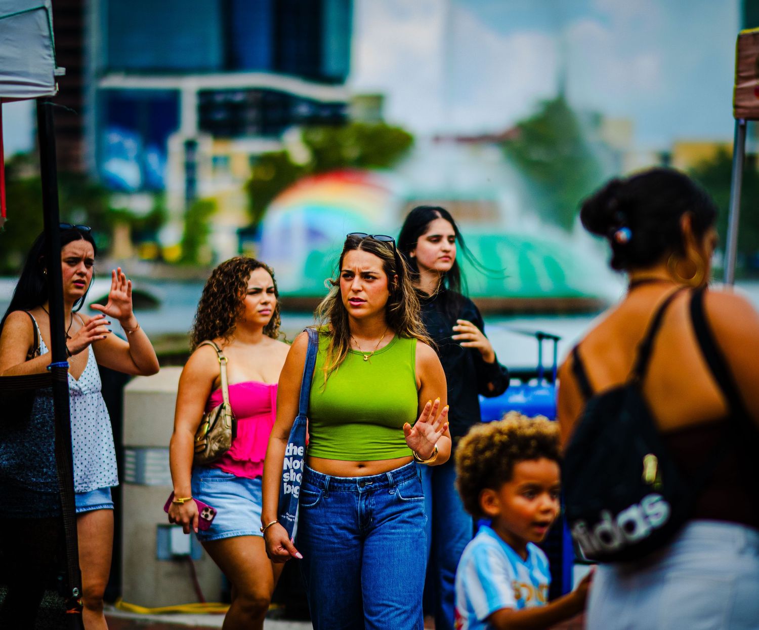 Group of young women walking on busy urban sidewalk, wearing casual summer outfits in city.