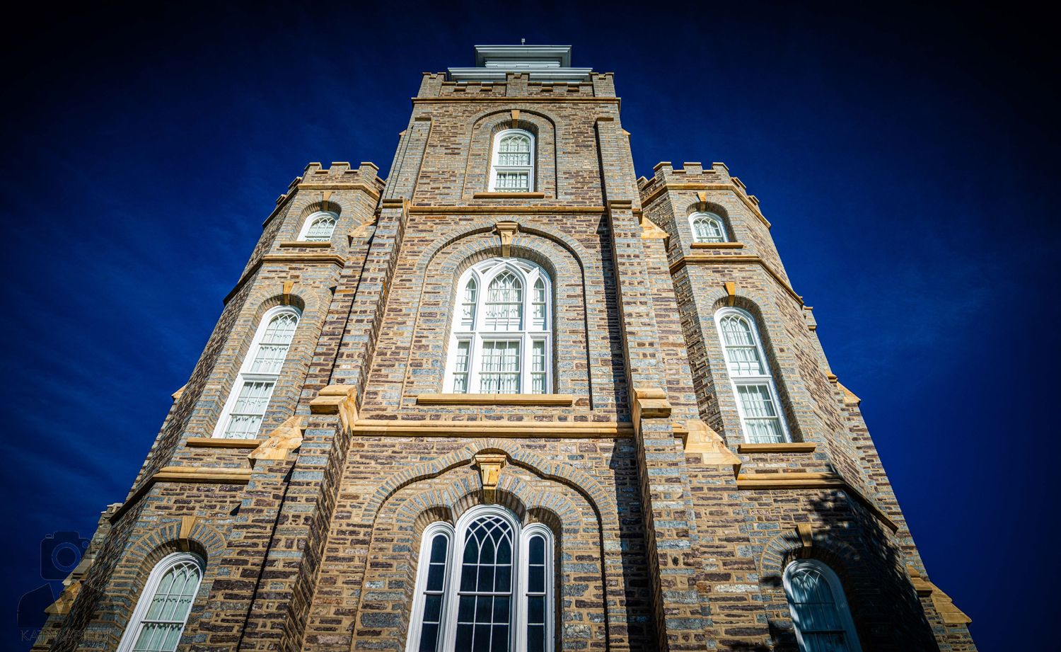 Gothic stone church facade with arched windows and towers against deep blue sky.