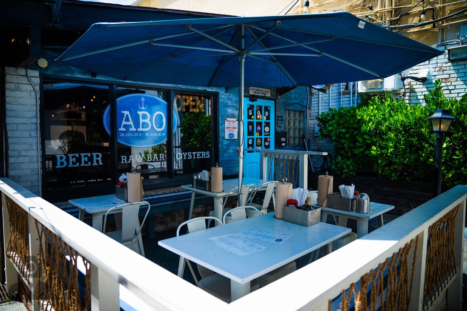 Blue patio umbrellas provide shade over outdoor seating at a restaurant storefront.